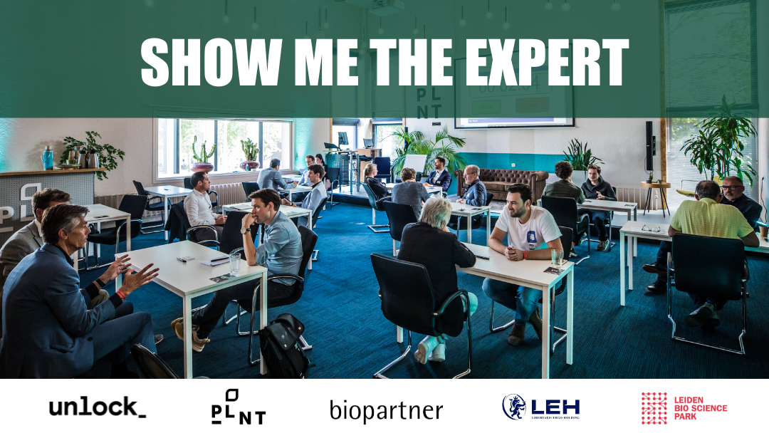 A room full of tables, at each table there are two people sitting across from each other talking. Above the picture is a banner stating 'Show me the expert'. Below are the logo's of the organising parties: unlock_, plnt, biopartner, LEH and Leiden Bio Science Park